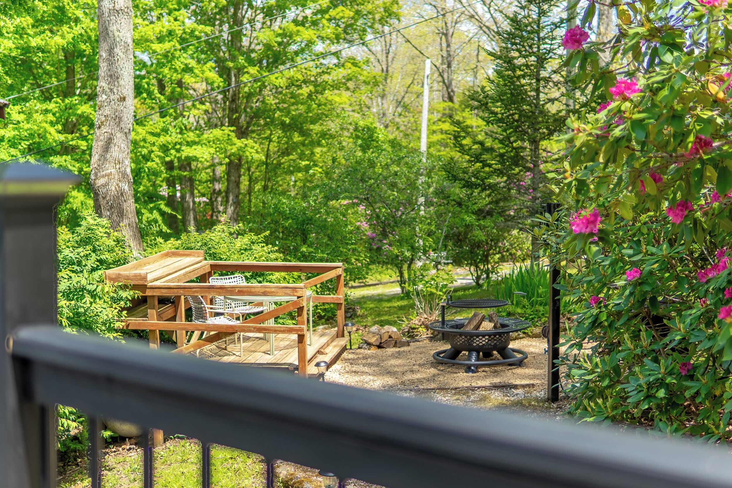 Une terrasse en bois avec une table et des chaises, entourée de verdure et agrémentée d’un foyer extérieur.