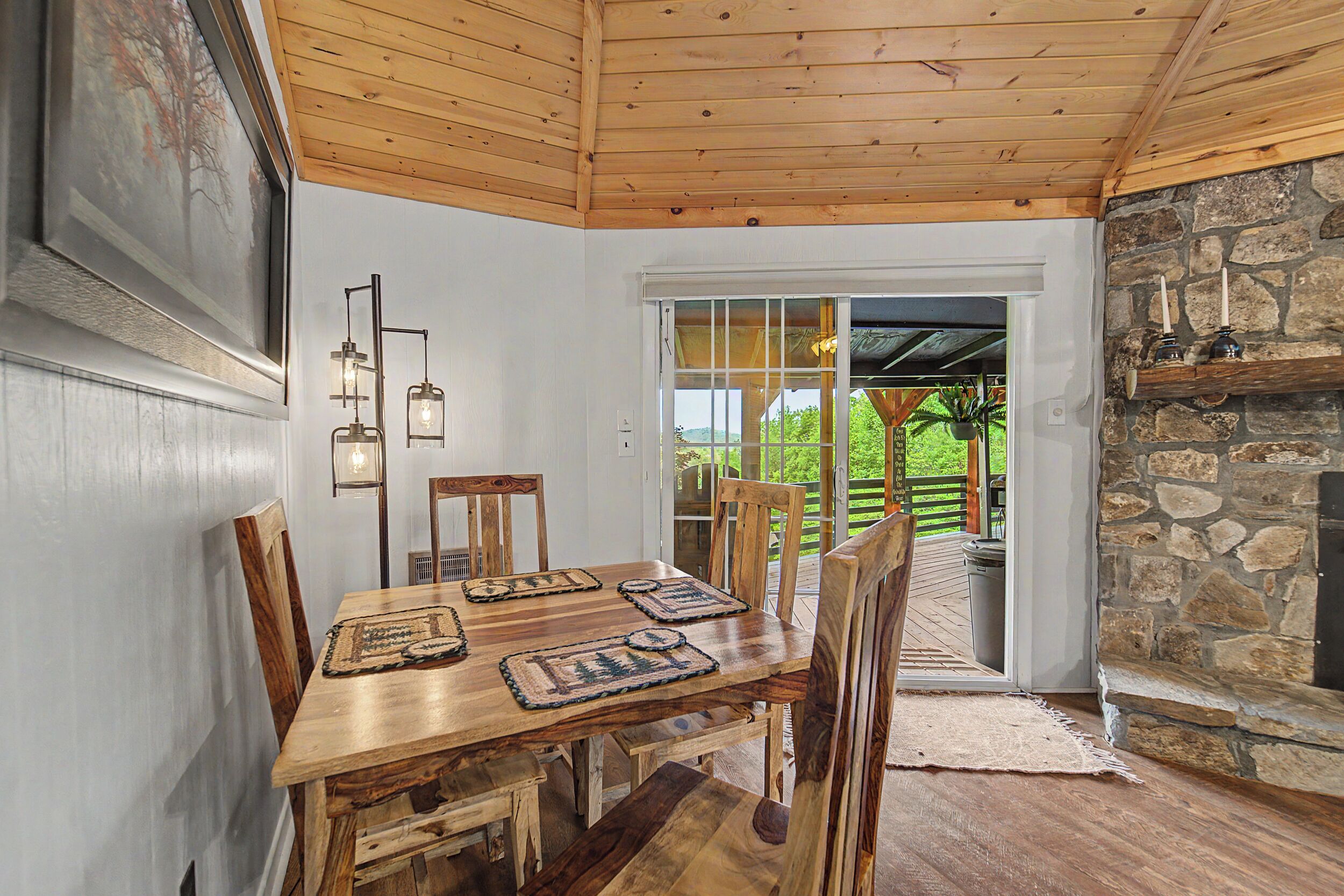 A wooden dining table with chairs, a stone fireplace, and a view of the outdoors.
