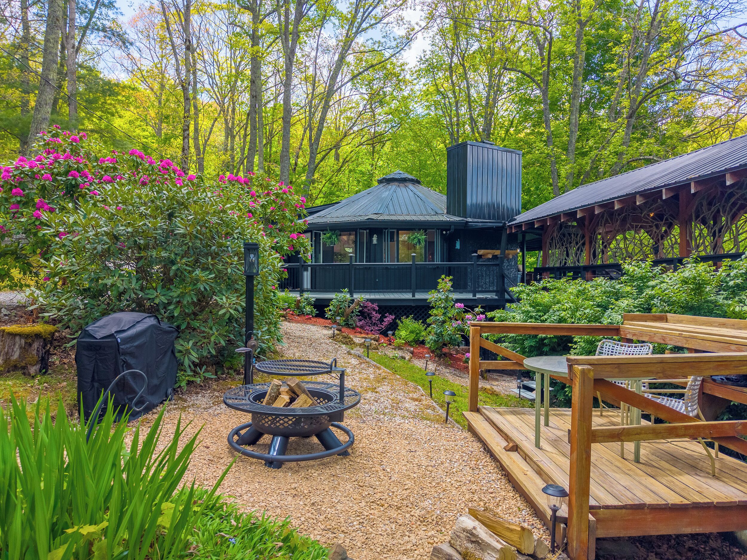 Een chalet met terras, omringd door een tuin met grindpaden en begroeiing.