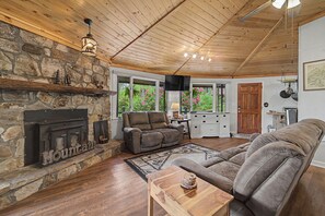 A cozy living room with a stone fireplace, wooden ceiling, and a comfortable sofa. - The Cullowhee Cabin | Restful Retreat | Mountain View | Fire Pit | Games (Cullowhee)