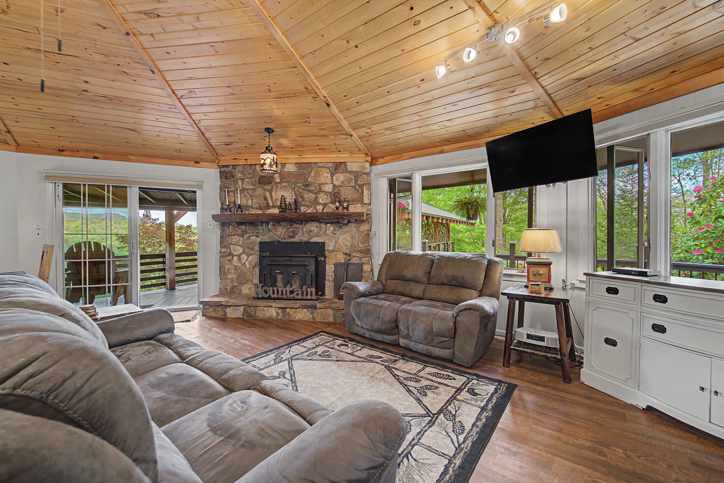 A cozy living room with a stone fireplace, leather sofa, and a television.