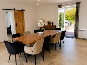 Ein Essbereich mit Holztisch, sechs Stühlen, einer Vase mit weißen Blumen, einem Holzschrank und einer Schiebetür, die auf eine Außenpatio führt.