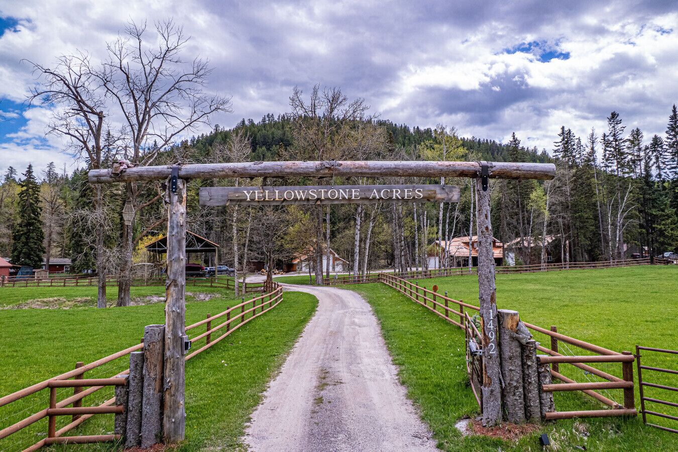A rustic wooden archway with 'Yellowstone Acres' sign, a gravel path, and a fenced area.