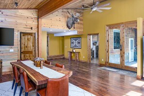 A spacious room with a wooden dining table, leather chairs, a mounted moose head, and a ceiling fan. - The Hidden Draw Retreat (Kalispell)