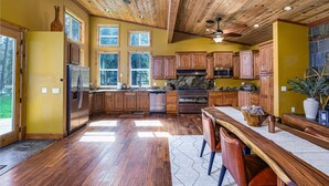 Una cocina con armarios de madera, un refrigerador de acero inoxidable, una estufa y un comedor con una mesa y sillas de madera.