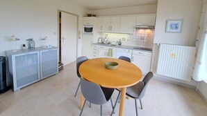 A compact kitchen with white cabinets, a microwave, and a sink. There is a dining table with chairs and a small cabinet with a microwave above it. - Cozy Apartment Near the Dunes (Koksijde)