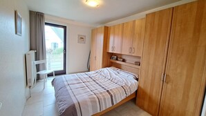 A bedroom with a bed, wooden wardrobe, a radiator, and a window with curtains. - Cozy Apartment Near the Dunes (Koksijde)