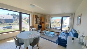 A spacious living area with a dining table, sofa, and TV. - Cozy Apartment Near the Dunes (Koksijde)