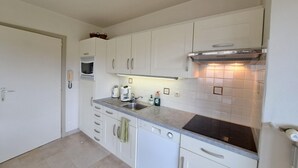 A compact kitchen with white cabinets, a built-in microwave, a gas stove, and a sink. - Cozy Apartment Near the Dunes (Koksijde)