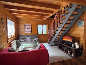 Un intérieur en bois avec un escalier, un canapé, un téléviseur et une horloge.