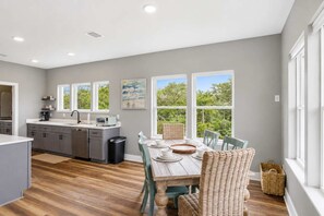 A modern kitchen with grey cabinets, a dining table with chairs, and large windows offering a view of trees. - New- Seabreeze-Bay Front -Pet Friendly (Eastpoint)