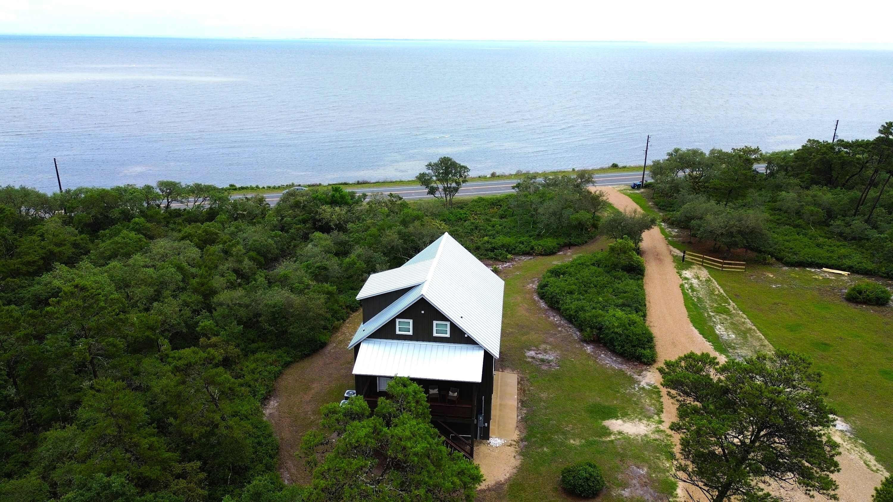 A house with a metal roof, surrounded by dense greenery and a dirt path leading to a road.
