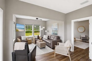 A modern living room with a sofa, armchairs, a coffee table, and a television. There are large windows with a view of the outdoors. - New- Seabreeze-Bay Front -Pet Friendly (Eastpoint)