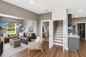 A modern living room with a sofa, armchairs, a coffee table, and a dining area with a kitchen in the background. - New- Seabreeze-Bay Front -Pet Friendly (Eastpoint)