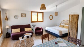 A cozy room with a sofa, armchair, and a bed with a wooden headboard. There's a round table with a checkered tablecloth and a lamp on a side table. - The Unusual Getaway • Nature Chalet & Hot Tub (Meilhac)