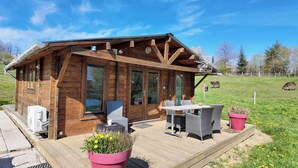 A wooden cabin with a deck, outdoor seating, and a view of a grassy field. - The Unusual Getaway • Nature Chalet & Hot Tub (Meilhac)
