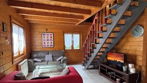 A wooden cabin interior with a staircase, a sofa, a television, and a clock. - Les Chalets de Meilhac • Chalet N°2 (Meilhac)