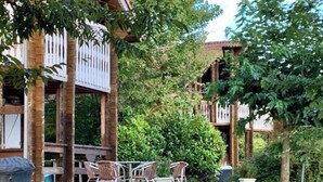 A building with a wooden facade, a covered outdoor seating area with chairs, and a white picket fence. - Les Chalets de Meilhac • Chalet N°2 (Meilhac)