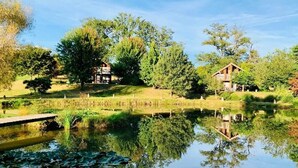 A serene lakeside setting with two wooden cabins, a wooden dock, and lush greenery. - Les Chalets de Meilhac • Chalet N°2 (Meilhac)