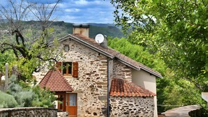 A stone building with a red-tiled roof, a satellite dish, and a stone wall.