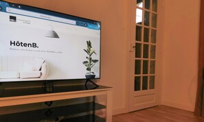 Une chambre d’hôtel avec un lit, une plante en pot et un téléviseur affichant un site web.