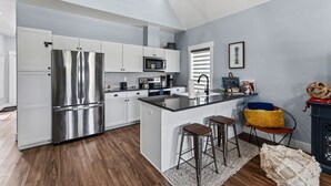 Una cocina moderna con electrodomésticos de acero inoxidable, muebles blancos y una isla central con taburetes de bar.