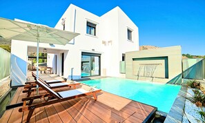 Ein modernes Haus mit Swimmingpool, Holzterrasse und Liegestühlen.