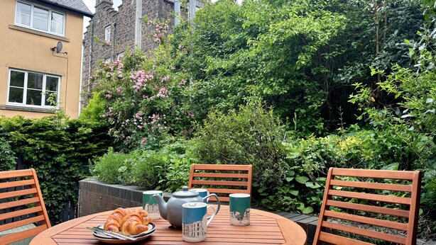 A round wooden table with a teapot, two mugs, and a plate of croissants. - Muriau Tref - Three Bedroom Cottage, Sleeps 4 (Conwy)