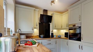 A modern kitchen with white cabinets, stainless steel appliances, and a wooden countertop. - Muriau Tref - Three Bedroom Cottage, Sleeps 4 (Conwy)