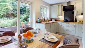A modern kitchen with a dining area, large windows, and a view of greenery. - Muriau Tref - Three Bedroom Cottage, Sleeps 4 (Conwy)