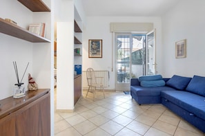 Ein Wohnzimmer mit einem blauen Sofa, einem Holzschrank, einem Sessel und einer Tür, die auf einen Balkon führt.