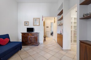 Ein Wohnzimmer mit einer Couch, Fernseher, einem Holzschrank und einem Flur, der zum Kochbereich führt.