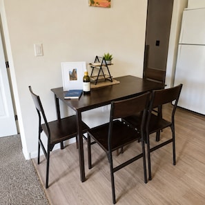 A dining area with a table, four chairs, a small plant, a wine bottle, and a framed picture.