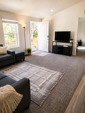 A living room with a sofa, a TV on a stand, a rug, and a door leading to an outdoor area.
