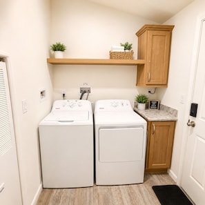 A laundry room with two front-loading washing machines, a wooden cabinet, and a shelf with plants.