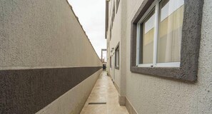 A narrow alleyway with a tiled floor, a window with a textured frame, and a door at the end. - Casa na Praia Grande a 600m da Praia do Caicara (PRAIA GRANDE)