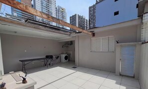 Ein Wohngebäude mit gefliestem Patio, einer Waschmaschine und einer Bank.