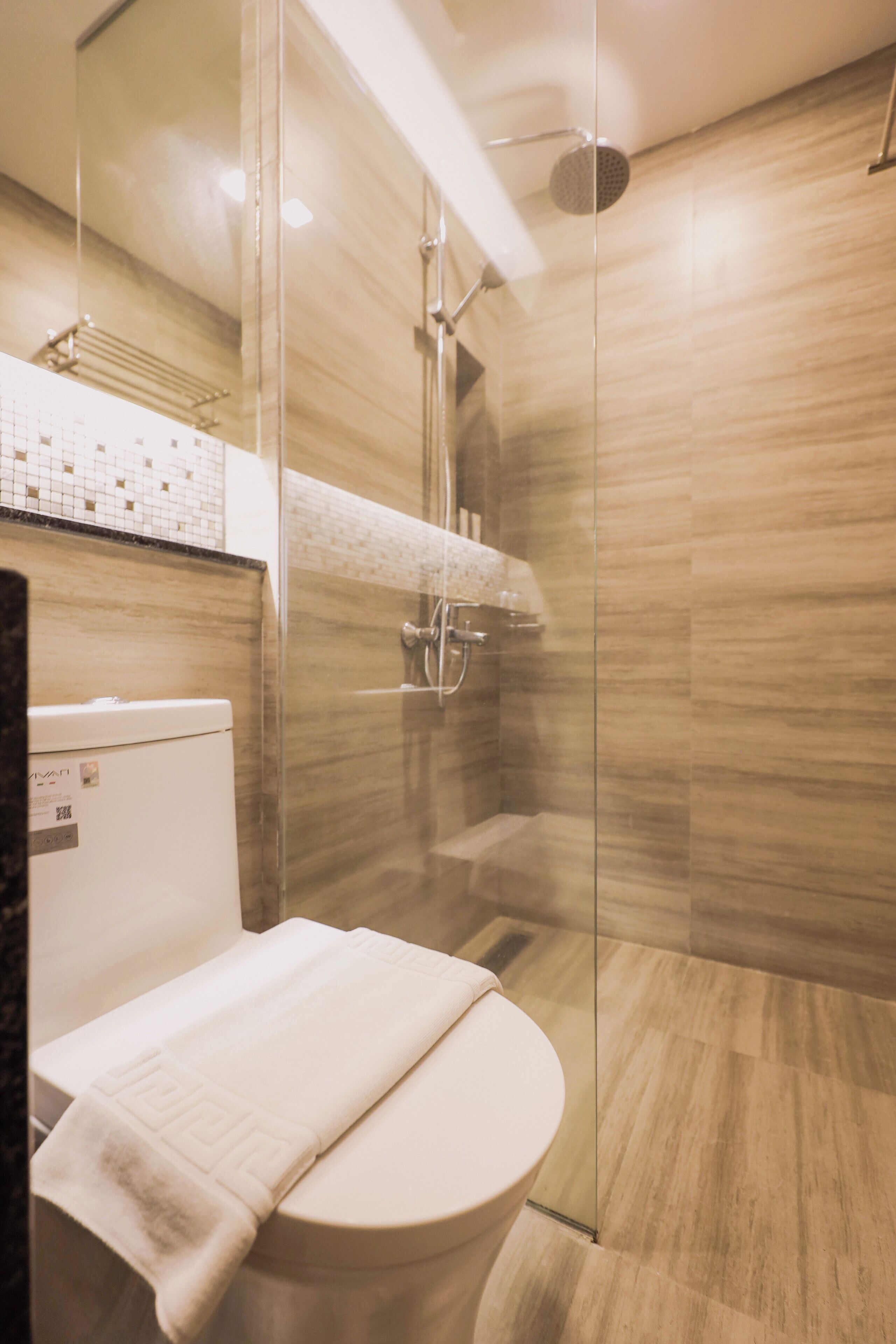Un baño moderno con cabina de ducha de vidrio, inodoro y una toalla en el suelo.