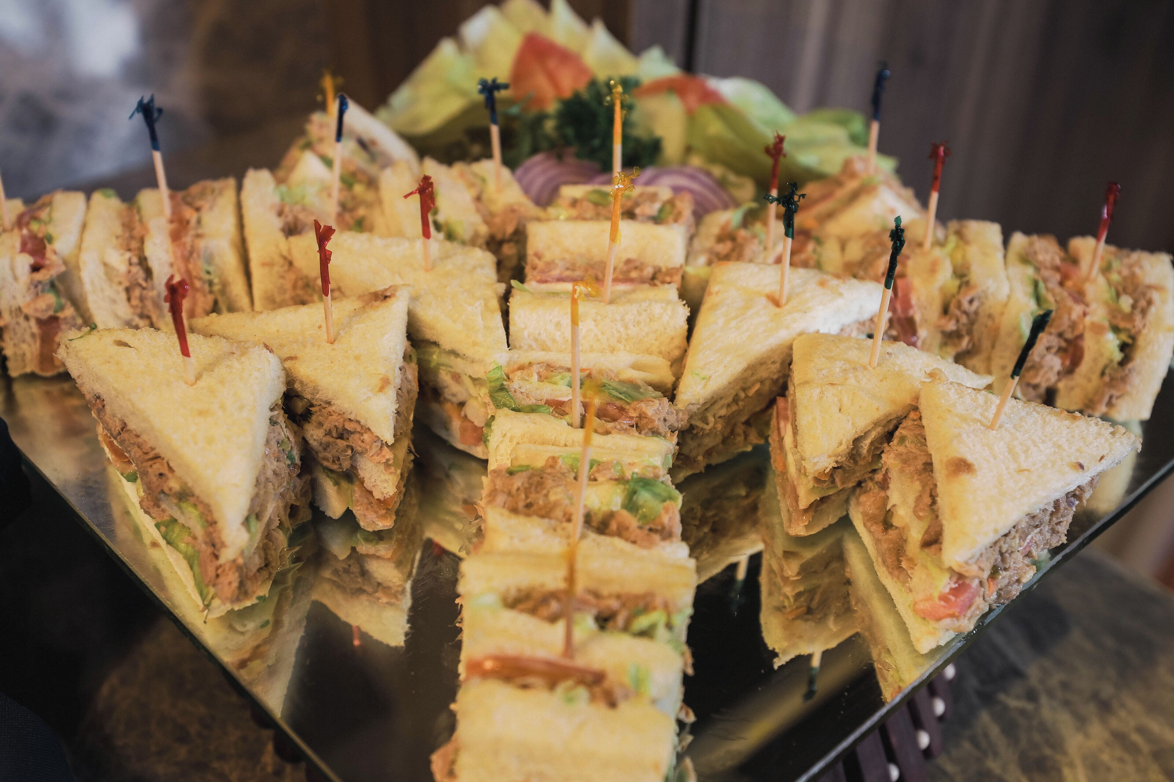 A tray of sandwiches with toothpicks, arranged on a metal surface.