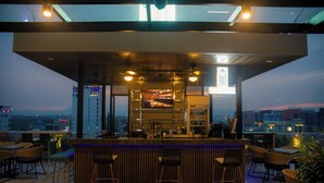 A rooftop bar with a bar counter, stools, and a city view. - El Vistra Hotel (Angeles City)