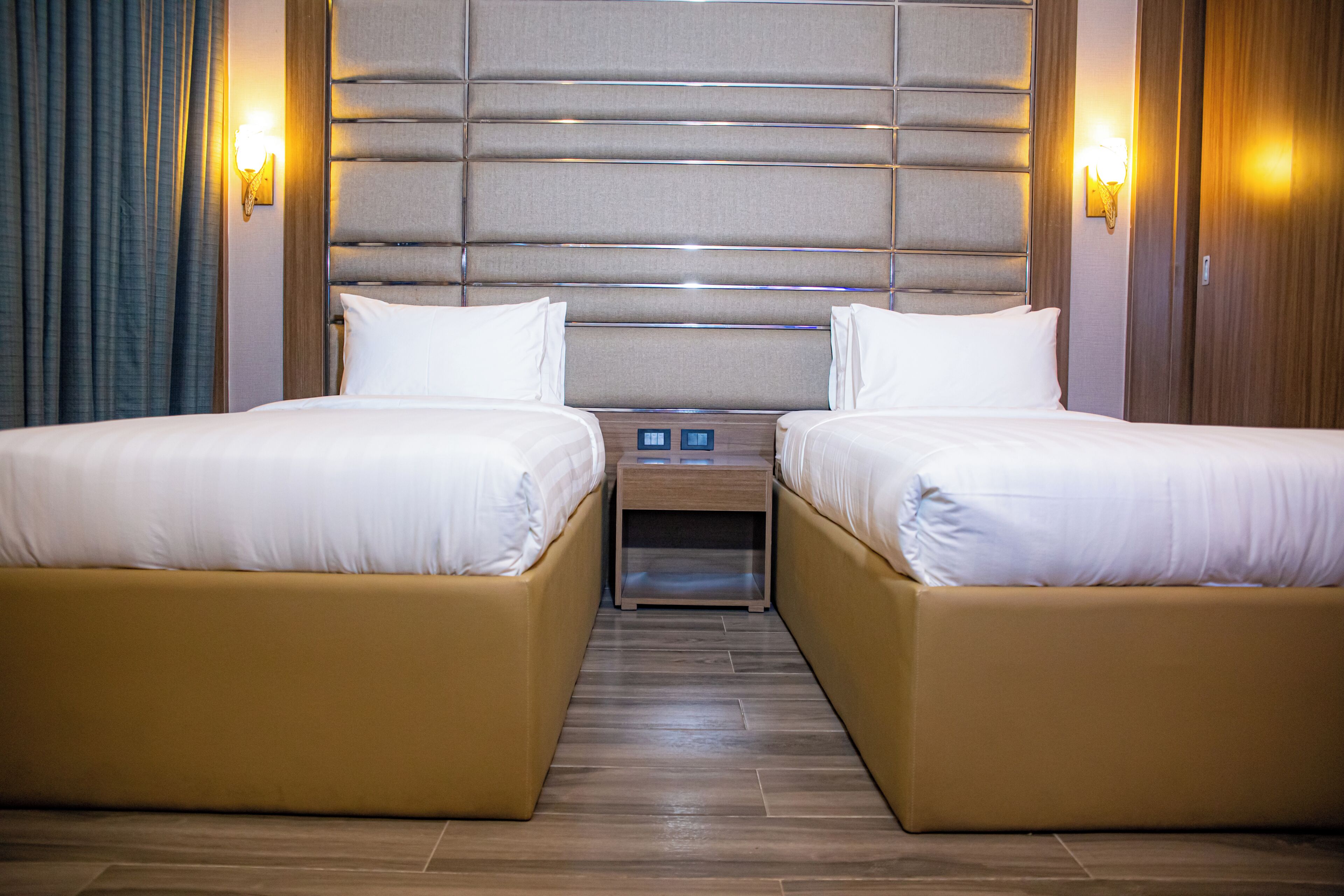 Une chambre d’hôtel avec deux lits, une tête de lit en bois, des lampes de chevet et une table de chevet.