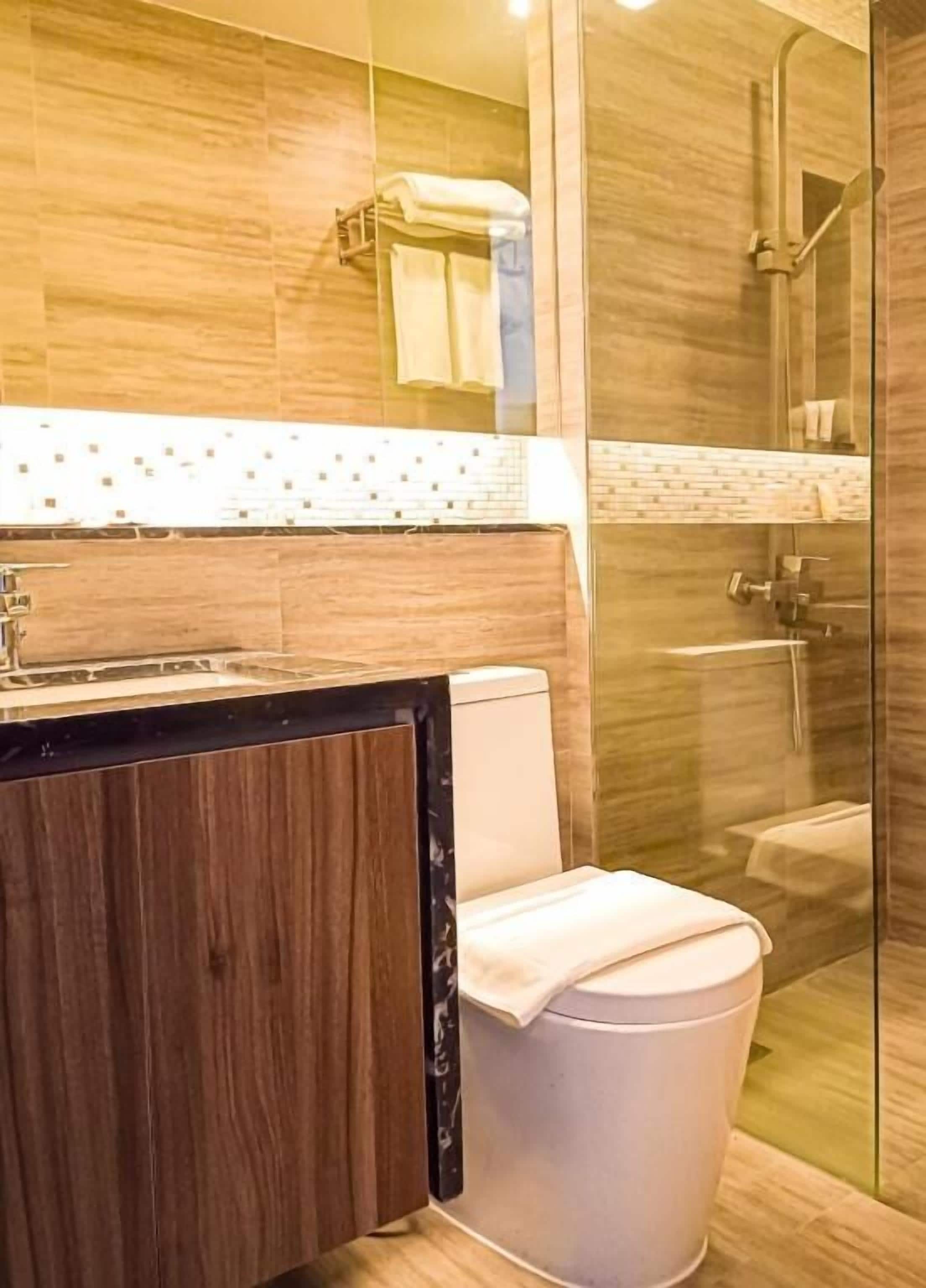 A bathroom with a wooden vanity, a toilet, and a glass shower enclosure.