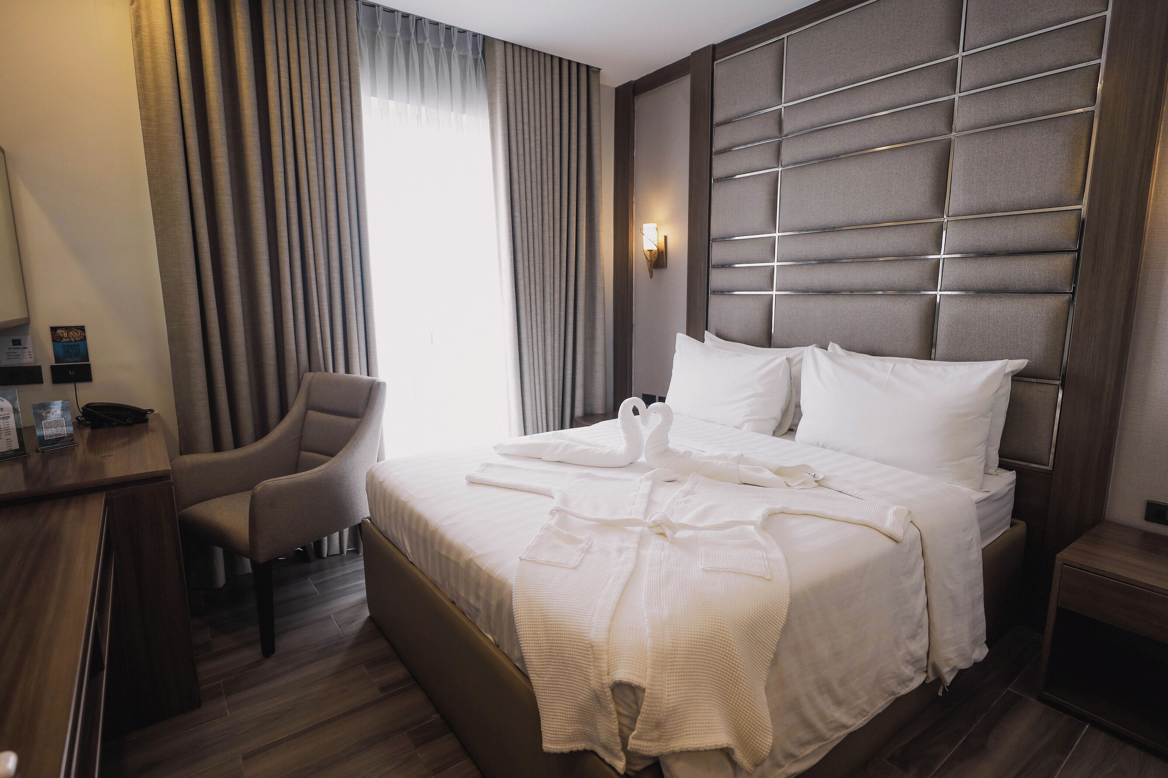 Hotellihuone, jossa on sänky, tuoli, työpöytä ja seinään kiinnitetty valaisin.