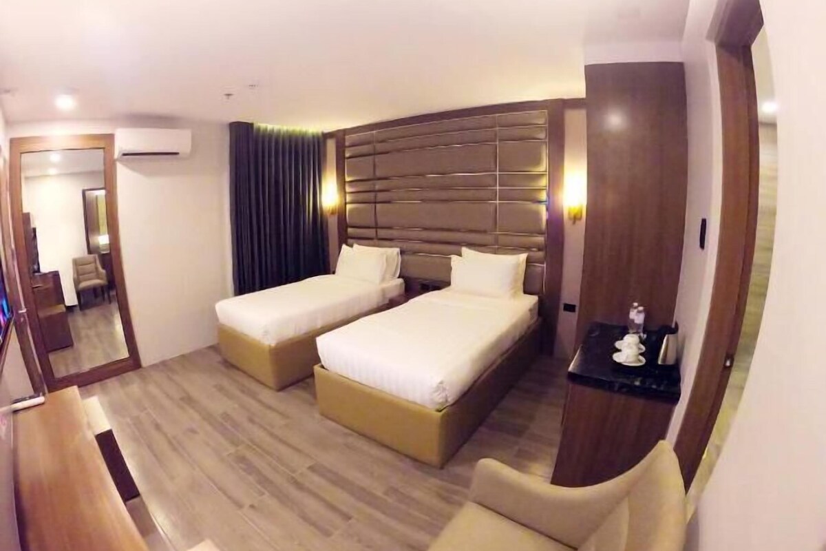 Ein Hotelzimmer mit zwei Betten, einem Schreibtisch, einem Stuhl, einem Spiegel und einem kleinen Tisch mit einem dekorativen Gegenstand.
