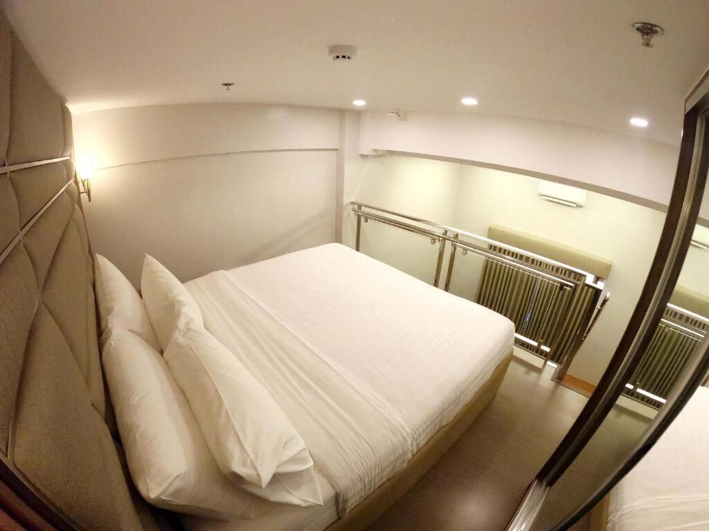 A hotel room with a bed, a headboard, a radiator, and a glass door.