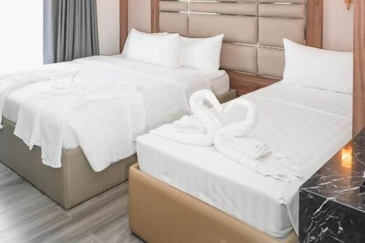 Ein Hotelzimmer mit zwei Betten, einem Holzkopfende, einem Marmornachttisch und einem Fenster mit Vorhängen.