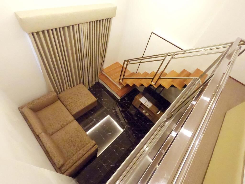 A modern staircase with a glass railing, a sofa, and a window with blinds.