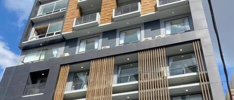 Un hotel de varios pisos con un diseño moderno, que cuenta con balcones, ventanas amplias y un logotipo destacado en la parte superior.