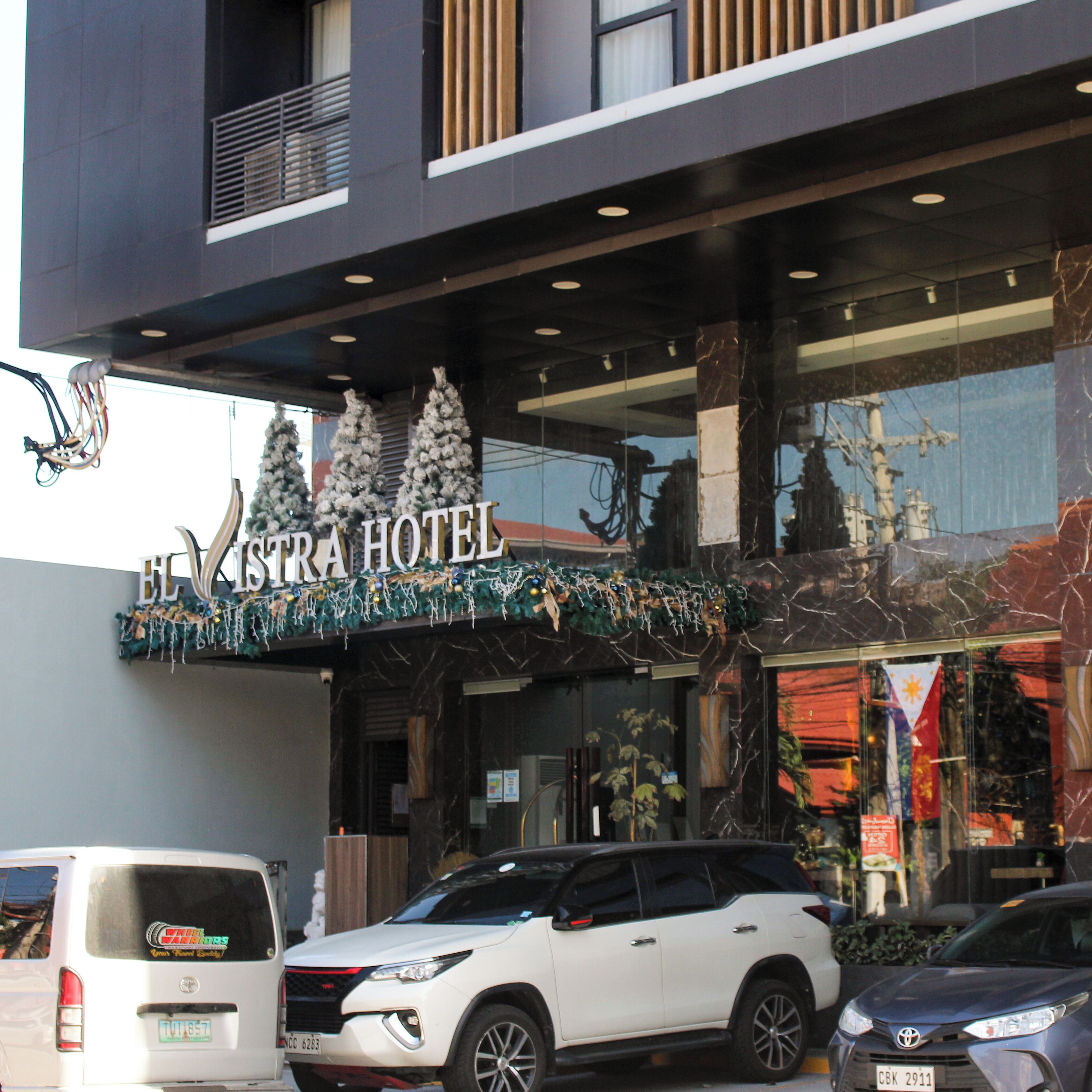 A hotel with a modern facade, a signboard, and a parking area with vehicles.