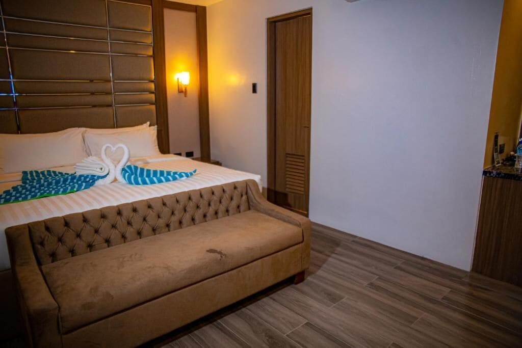 Una habitación de hotel con una cama, un sofá, una lámpara fijada en la pared y una puerta de madera.